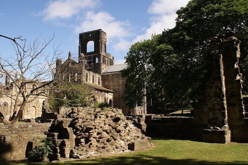 An ancient stone structure with a bell tower, surrounded by trees and grassy areas. 2