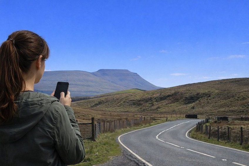 A person taking a photo of a winding road with a mountain in the background. 1