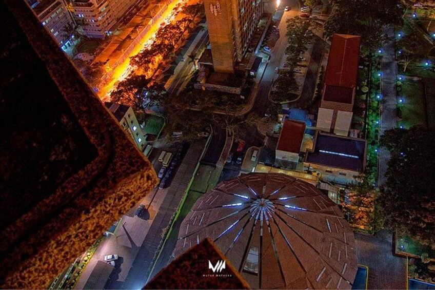 A cityscape at night with illuminated buildings, a large circular structure, and a prominent tower. 3