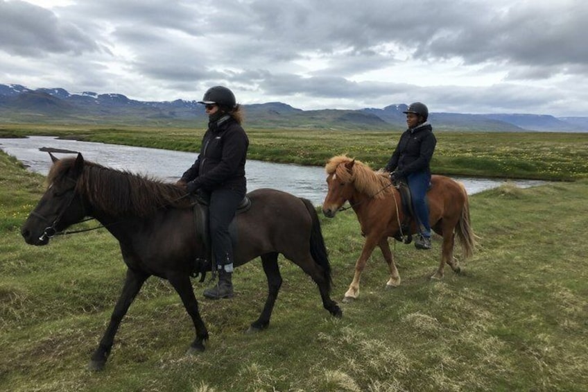 Deux personnes à cheval, évoluant sur un champ herbeux, avec une rivière et des montagnes en arrière-plan. 4