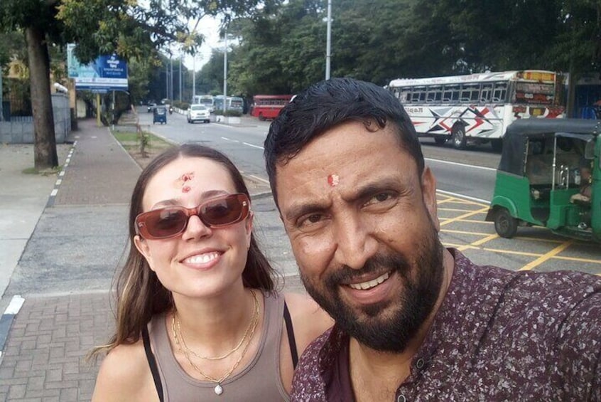 Ein Mann und eine Frau machen ein Selfie auf einer Stadtstraße, im Hintergrund ist ein Bus und ein Rikshaw zu sehen. 4