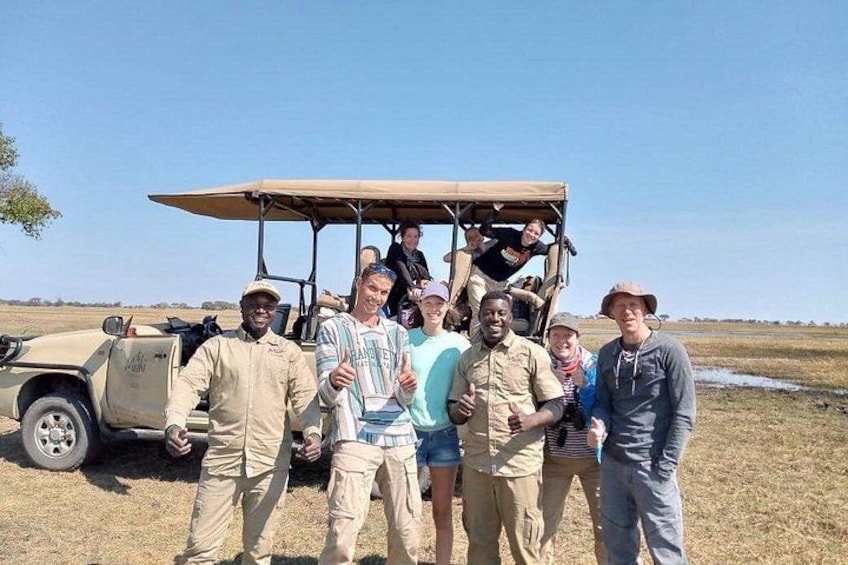 A group of people standing in a dry grass field with a vehicle in the background. 1