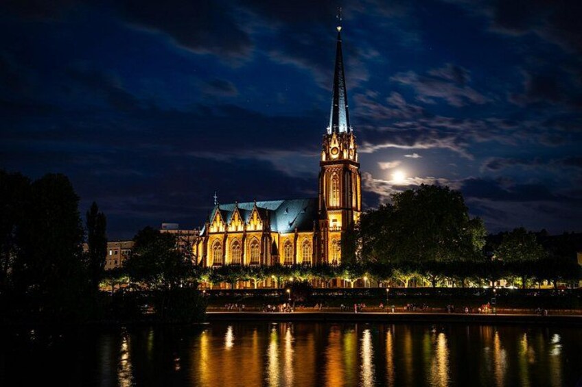 A cathedral with a tall spire, illuminated by lights, reflecting on a body of water. 1