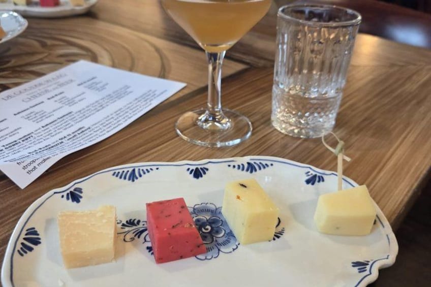 A plate with various cheese cubes, a glass of amber-colored liquid, and a menu on a wooden table. 5