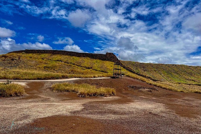 A gravel path leading to a metal structure on a hill with sparse vegetation under a partly cloudy sky. 4