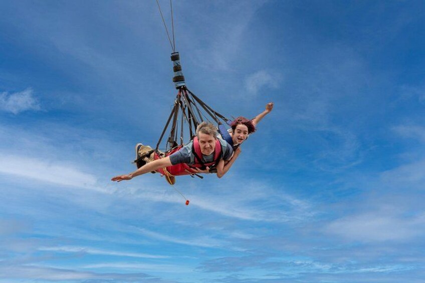 A person suspended in mid-air by a harness, attached to a cable system, against a clear blue sky. 4