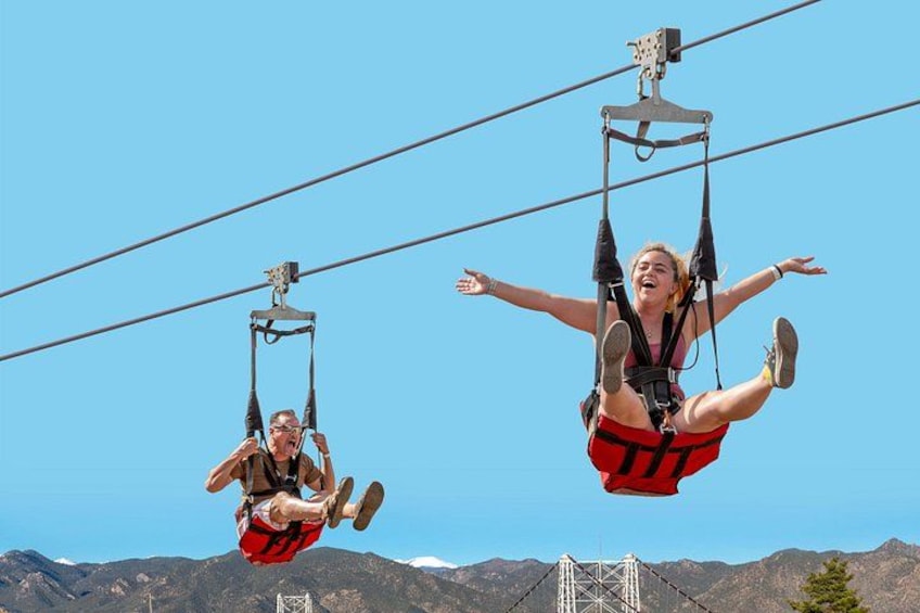 Two people suspended in the air on a cable system, with mountains in the background. 3
