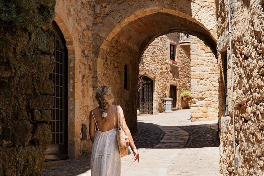 A woman in a white dress walking through an arched stone corridor with a rustic building in the background. 2