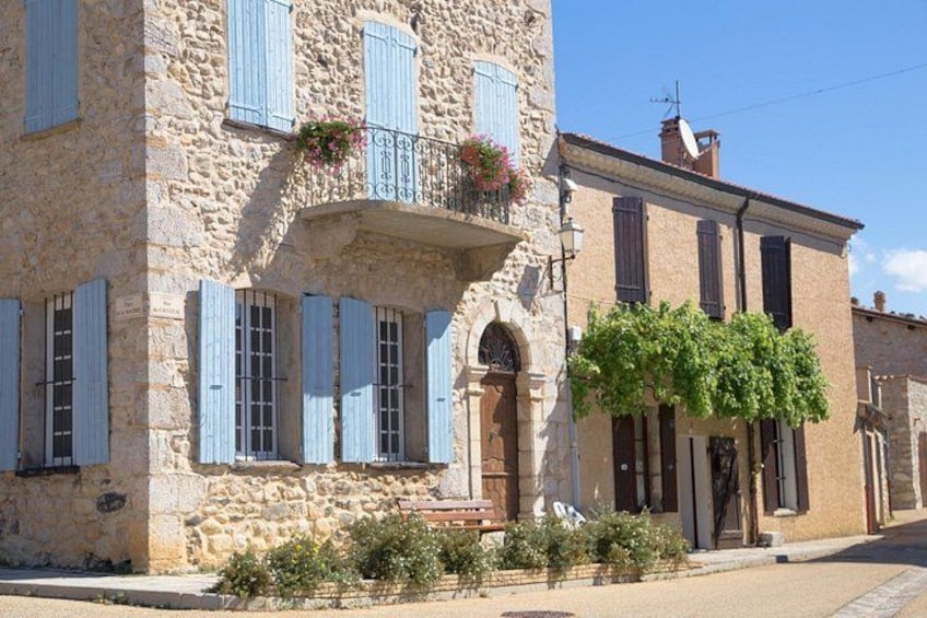 A stone building with blue shutters, a balcony with flowers, and a vine-covered wall. 4
