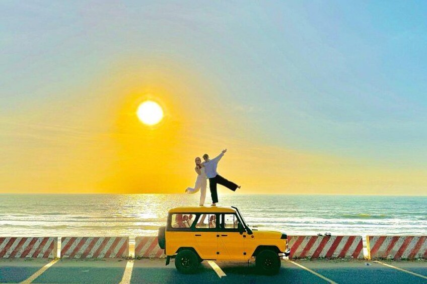 A yellow car parked on a road with a sunset in the background. 1