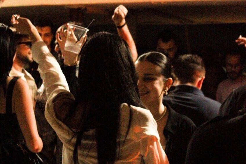 A crowded indoor event with people dancing and holding drinks. 1