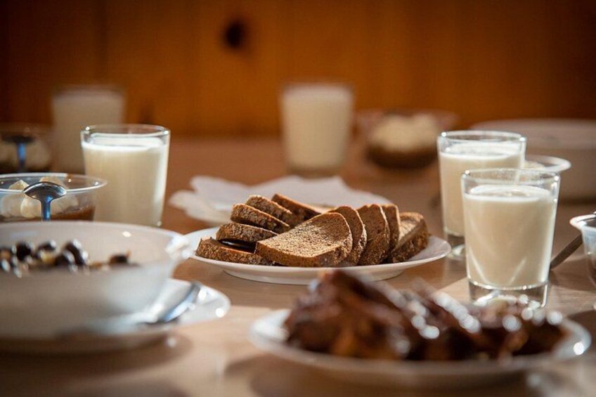 En frukostuppsättning med skivad bröd, mjölk och en tallrik med vad som ser ut att vara chokladöverdragna nötter. 4