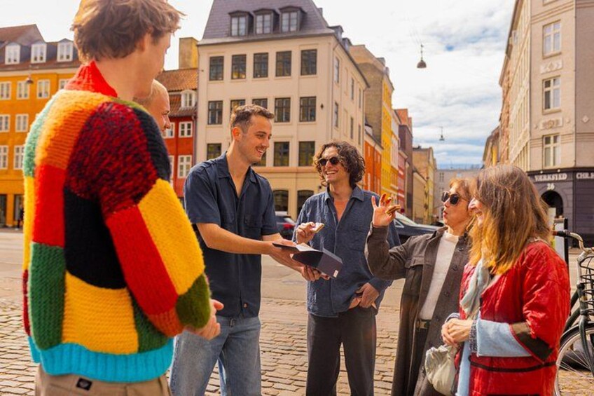 En grupp människor står på en kullerstensgata och samtalar. 3