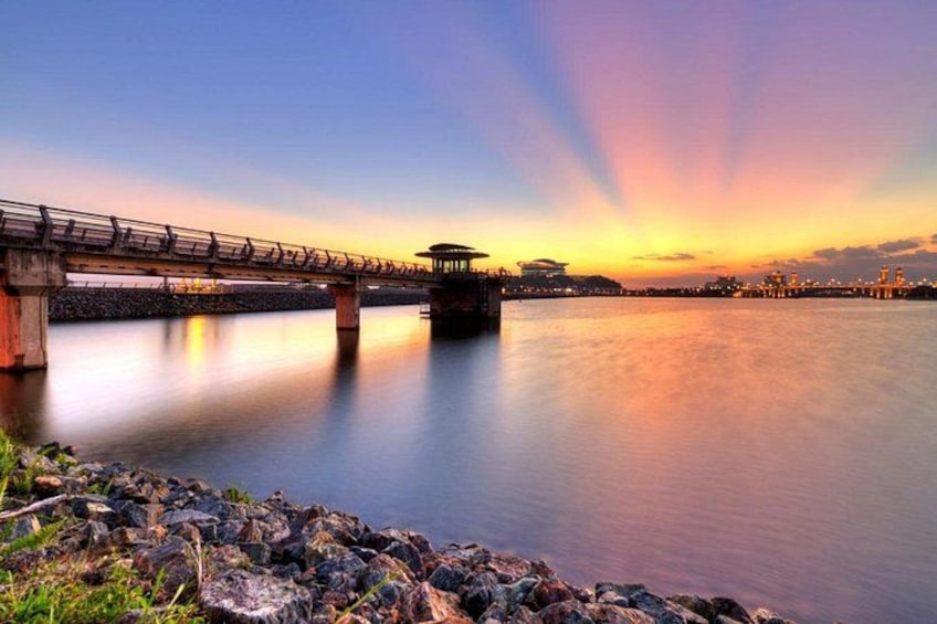 A bridge over calm water at sunset with a cityscape in the background. 4