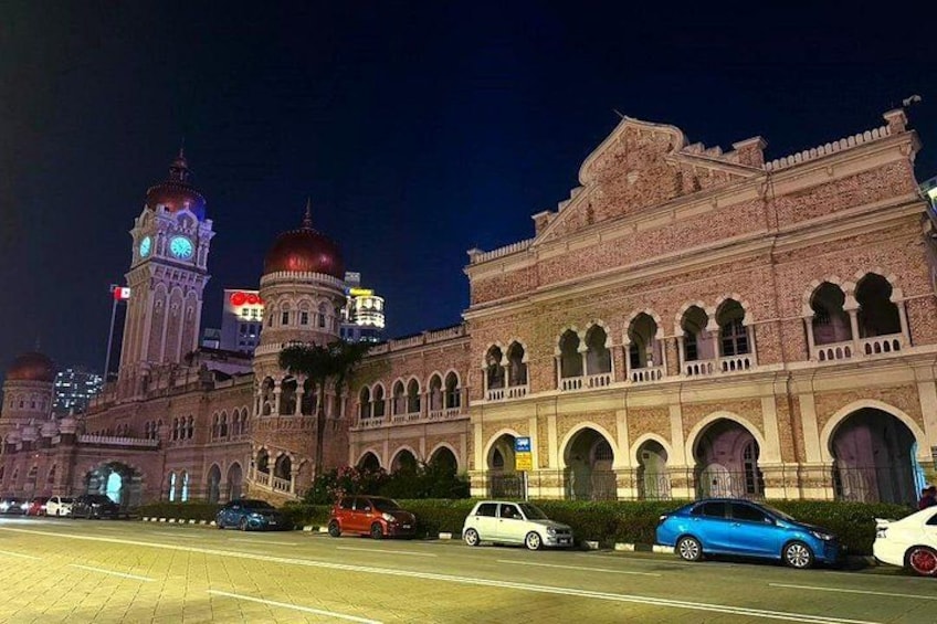 A historic building with arched windows and domed roofs, surrounded by parked cars and a clock tower in the background. 5