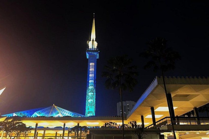 A tall tower with a pointed spire, illuminated blue lights, and a large building with a modern design in the foreground. 2