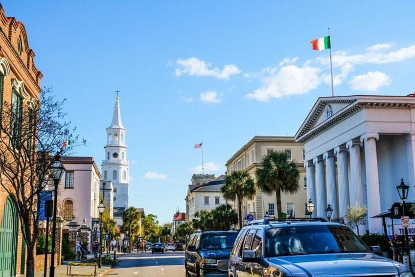 A street with historic buildings, a church tower, and a flag. 4