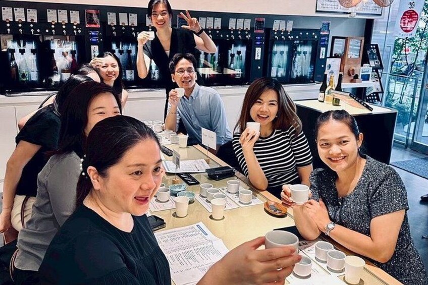 Un grupo de personas sentadas alrededor de una mesa, con tazas y papeles, en una cafetería con una barra y pizarras con el menú al fondo. 4