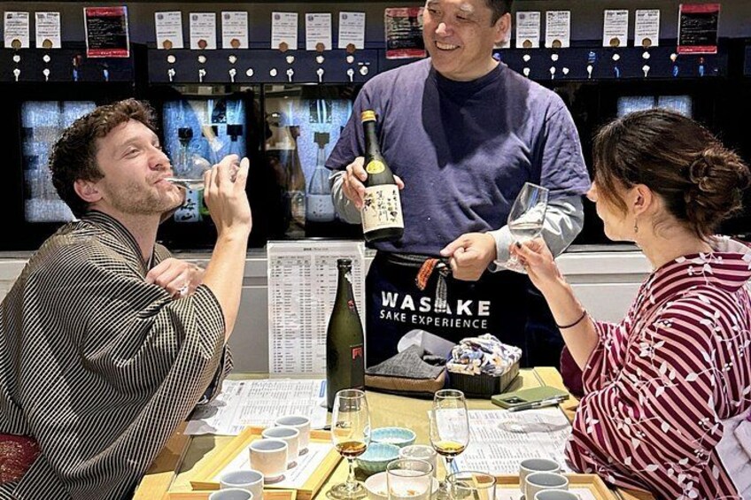 Tres personas sentadas a una mesa con una botella de vino, copas y un menú. 5