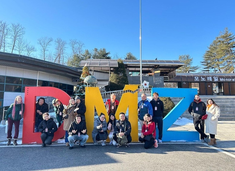 A group of people posing in front of large colorful letters spelling 'DMZ'. 1