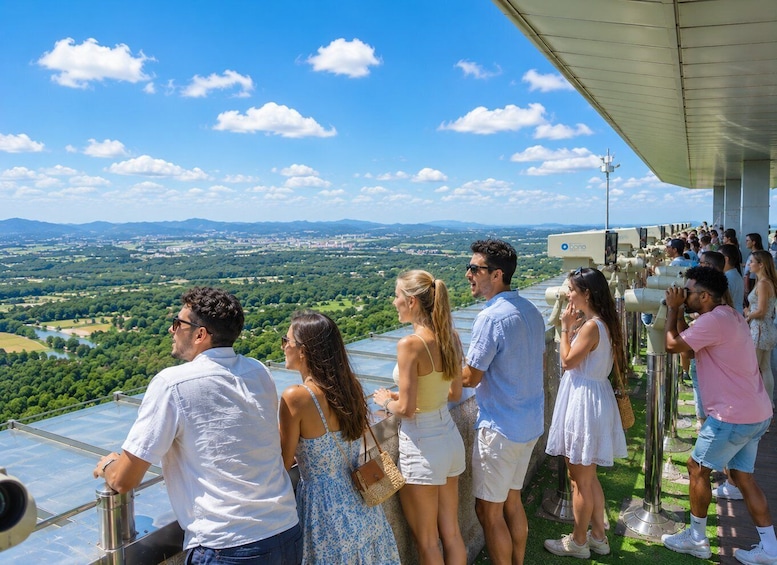 A group of people using telescopes to view a landscape with a river and mountains in the distance. 5