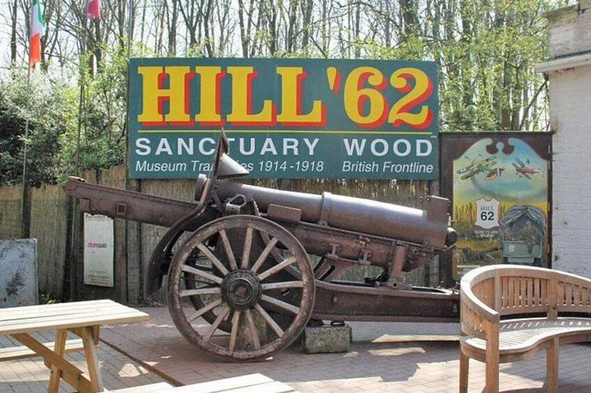 A cannon, a wooden table, a wooden chair, and a sign for Hill '62 Sanctuary Wood. 3