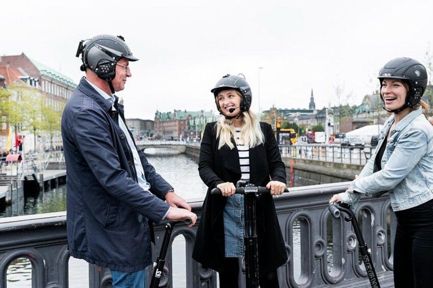 Three people on a bridge, one on a scooter, with a river and buildings in the background. 5