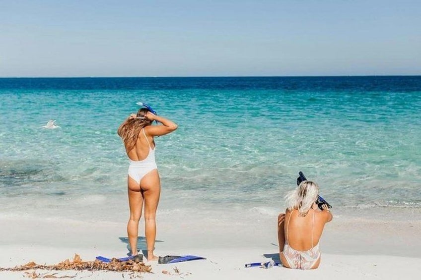 A beach with clear turquoise water, a person standing and another sitting with a camera. 4