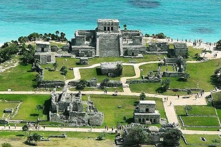 An ancient Mayan ruin complex with large stone structures and a clear view of the ocean. 1