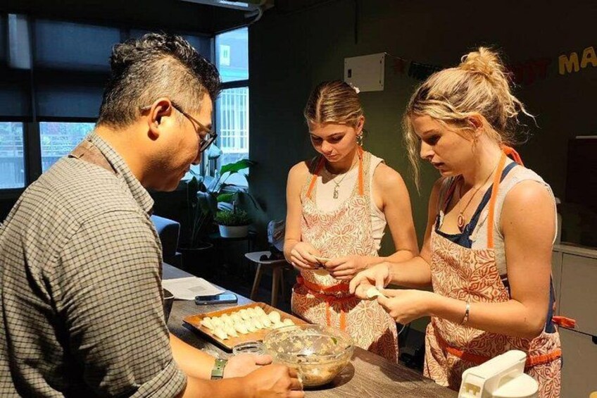Three people preparing food, with a bowl of ingredients and a tray of food items on the table. 2