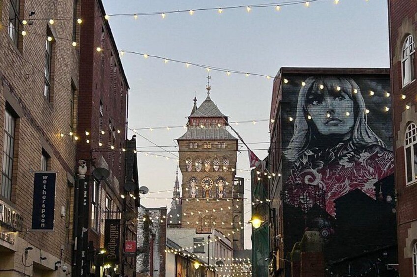 A street with string lights, a clock tower, and a mural. 2