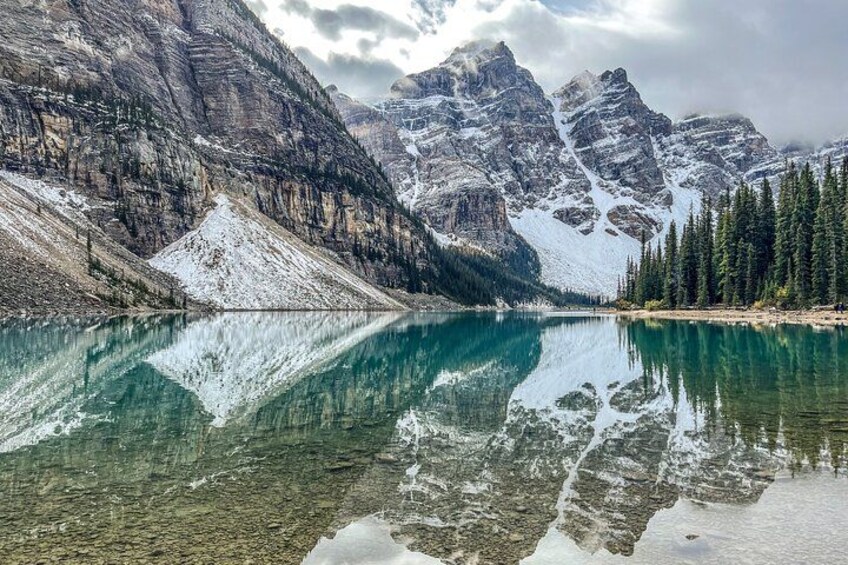Un lago de montaña con reflejos cristalinos, picos nevados y un bosque denso. 4
