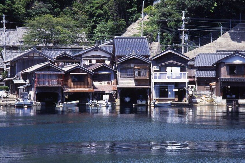 Traditional Japanese houses by a calm river, wooden boats docked, and a hilly landscape in the background. 2