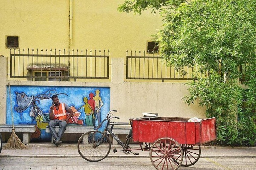 Una bicicleta con un carro rojo, un mural en una pared y una persona sentada en un banco. 5