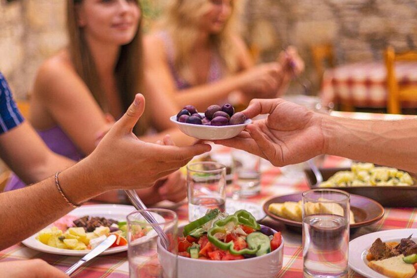 A group of people at a table with various dishes, including a salad and a plate with olives. 2