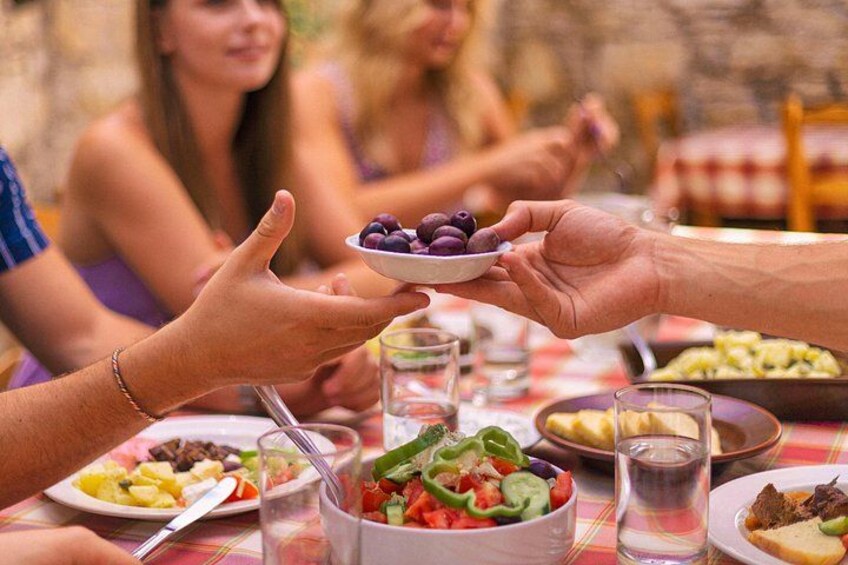 Un grupo de personas sentadas a una mesa con diversos platos, incluyendo una ensalada y un plato de aceitunas. 3
