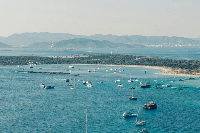 A coastal area with numerous boats anchored in the water, a sandy beach, and distant mountains. 2