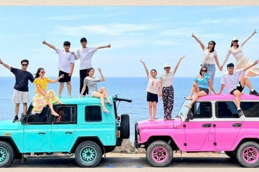 Ein türkisfarbenes und ein pinkfarbenes Geländefahrzeug sind auf einem Strand geparkt, auf denen Menschen stehen. 4