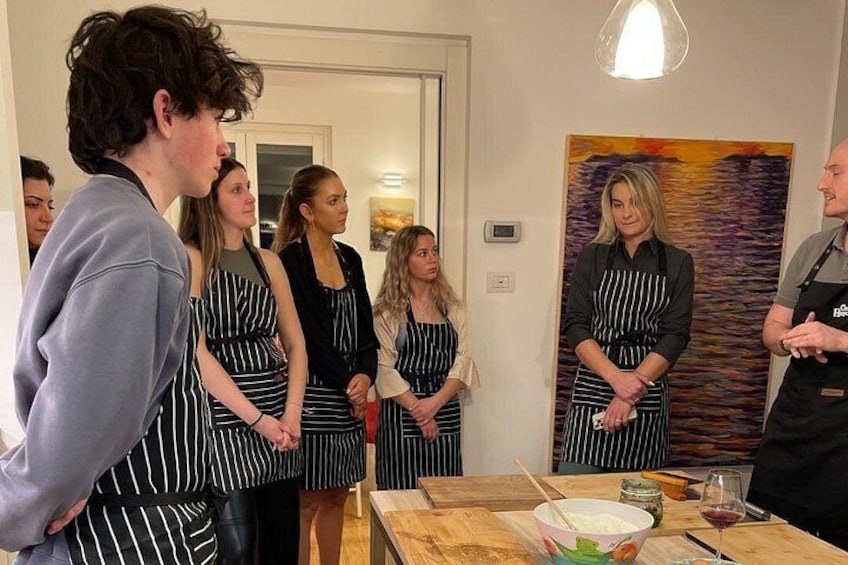 Un grupo de personas con delantales, una mesa con utensilios de cocina y un cuadro en la pared. 4