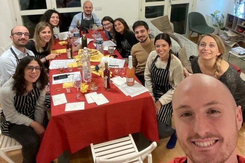 Un grupo de personas sentadas alrededor de una mesa con mantel rojo, varias botellas, copas y papeles. 5