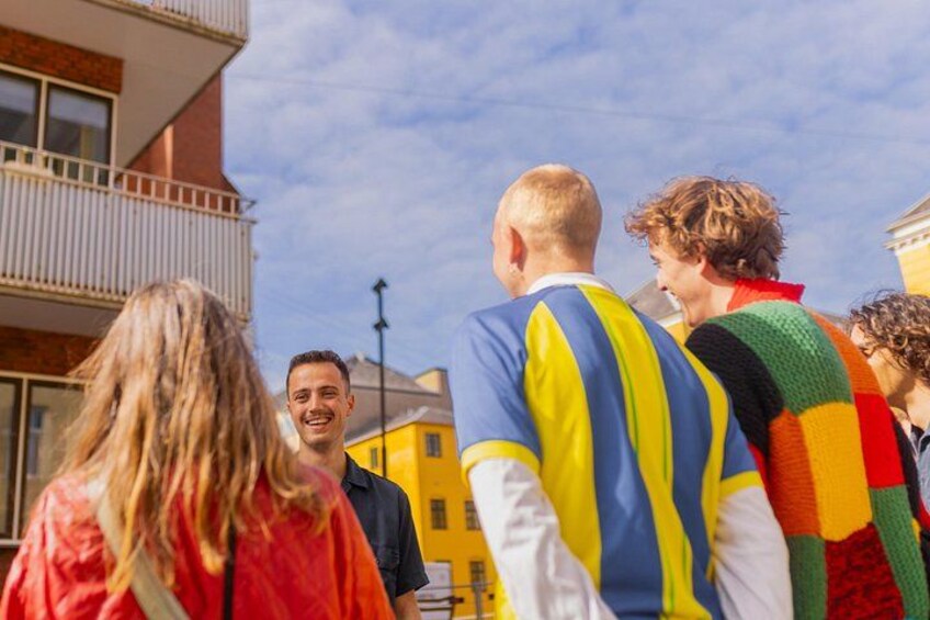 A group of people standing outdoors, a building with a yellow facade, and a clear sky. 5