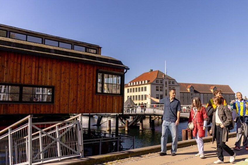 A wooden building with a ramp leading to a dock, a bridge, and a group of people standing by the water. 2