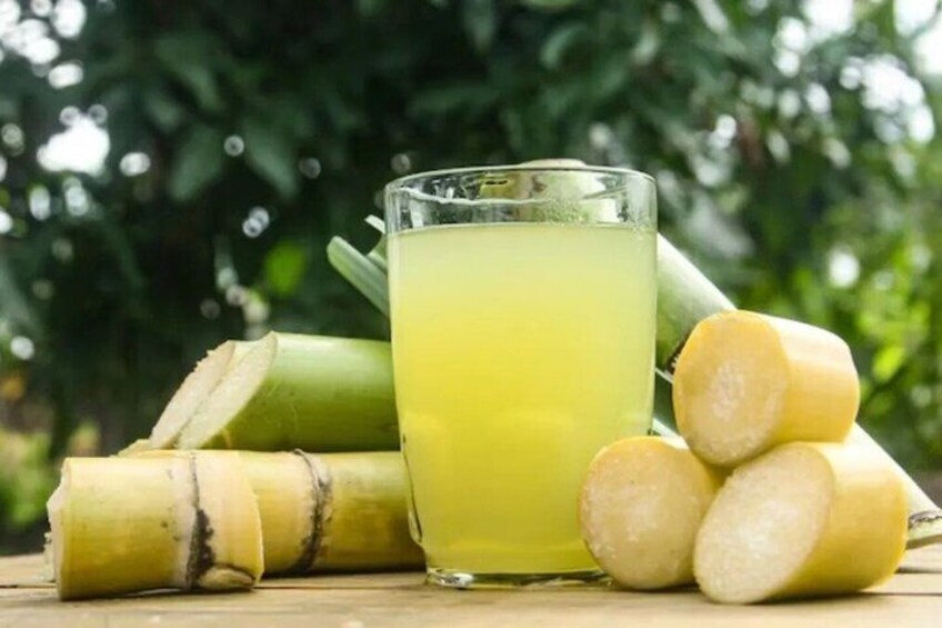 A glass of yellow liquid, likely ginger juice, with ginger roots and slices in the foreground, set against a blurred green background. 5