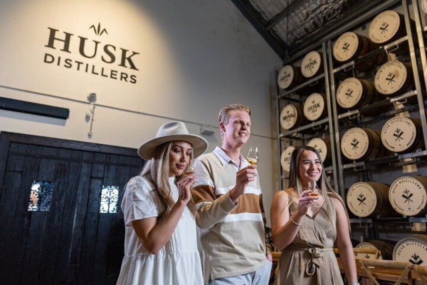 Three people in a distillery with barrels in the background. 3