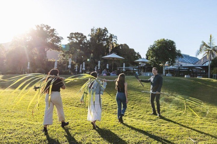 People playing with a rope on a grassy field with trees and buildings in the background. 2