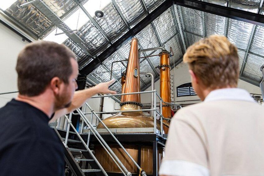 Two people inspecting a large copper distillation apparatus in an industrial setting. 2