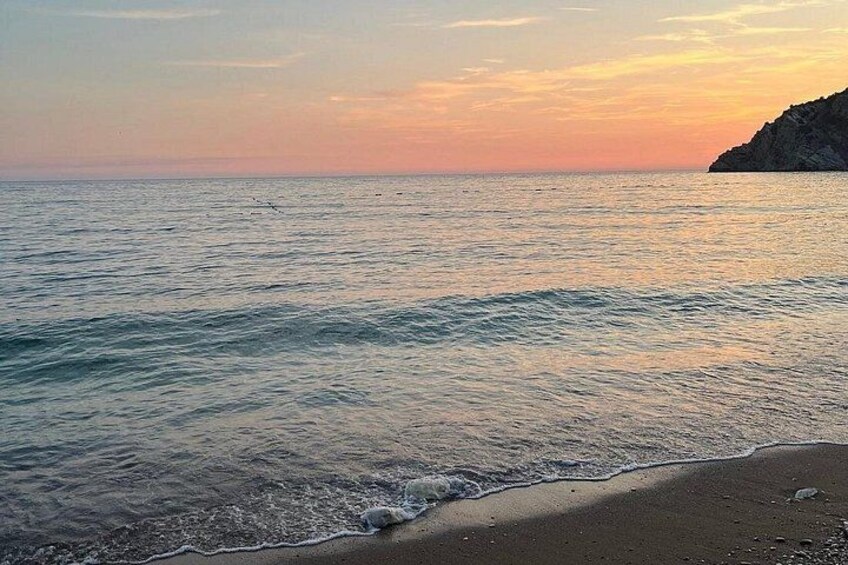 Una playa con agua tranquila, una orilla arenosa y un promontorio rocoso a lo lejos. 3