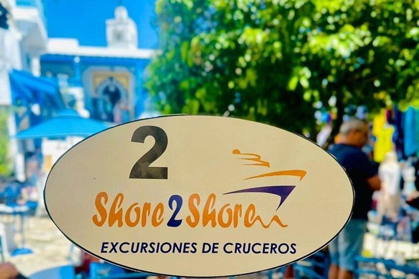 A sign with the number 2 and the text 'Shore2Shore Excursiones de Cruces' against a busy outdoor background. 3