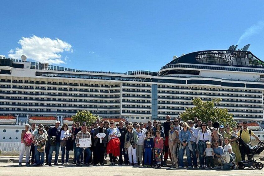 A group of people standing in front of a cruise ship. 1