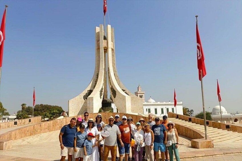 A group of people standing in front of a monument with a central spire and multiple red flags. 4
